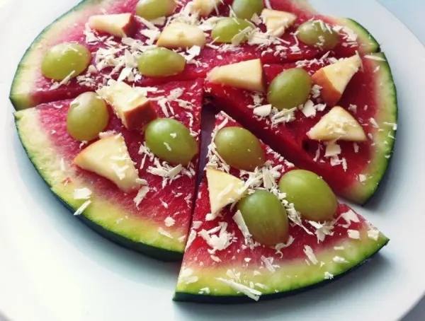 Melonen-Pizza: Wassermelonenscheiben belegt mit Weintrauben und Apfelstücken auf einem Teller, wie eine süße Pizza angerichtet.