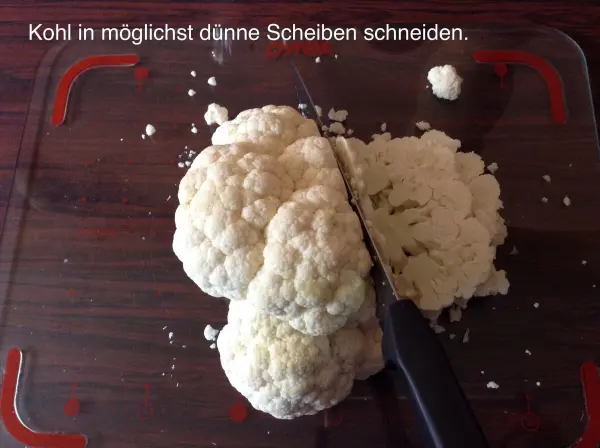 Kohl wird mit einem Messer in dünne Scheiben geschnitten, während er auf einem Holzbrett liegt.