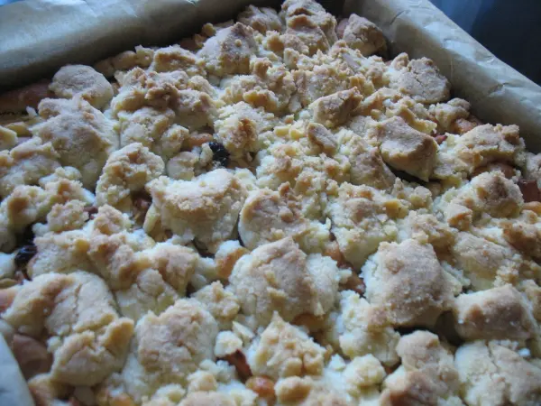 Ein goldbrauner Apfelkuchen mit Butterstreuseln befindet sich in einer Backform und wartet darauf, serviert zu werden.