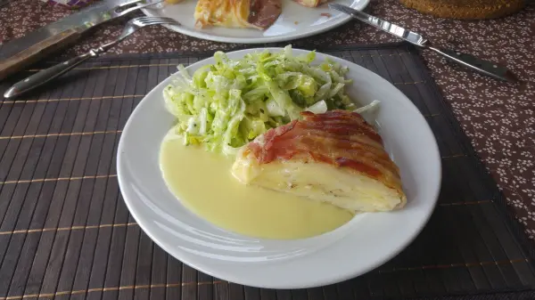 Ein Stück Kartoffel-Bacon-Kuchen liegt auf einem Teller, umgeben von frischem Salat und einer cremigen Sauce.