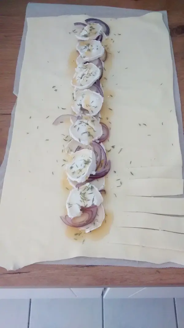 Ziegenkäse und Thymian sind auf einem ausgerollten Teig platziert, bereit zum Falten zu einem leckeren Zopf.