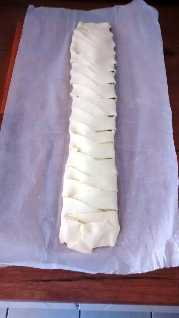 Ein Zopf aus Teig liegt auf Backpapier, geflochten und bereit zum Backen, um einen Ziegenkäse-Thymian-Honig-Zopf zu werden.