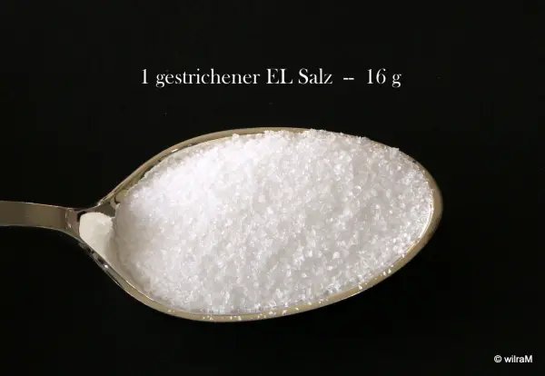 Ein Löffel mit geschnittenem Salz zeigt präzise 16 g Salz, auf schwarzem Hintergrund abgebildet.