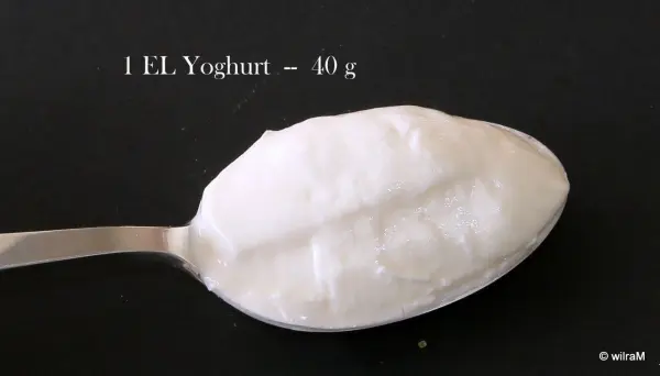 Ein Löffel Joghurt zeigt die Menge von 80 g und wird auf einem schwarzen Hintergrund abgemessen, ohne Waage.