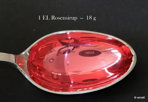 Ein Esslöffel mit rotem Sirup hält ca. 18 g, platziert auf einem schwarzen Hintergrund zur Veranschaulichung.