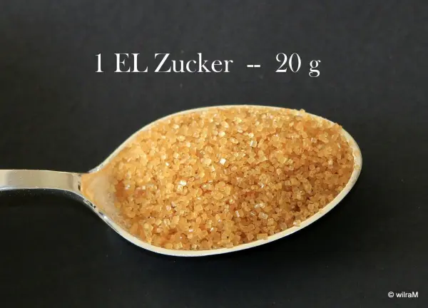 Ein Esslöffel mit braunem Zucker liegt vor schwarzem Hintergrund, beschriftet mit "1 EL/Zucker - 20 g".