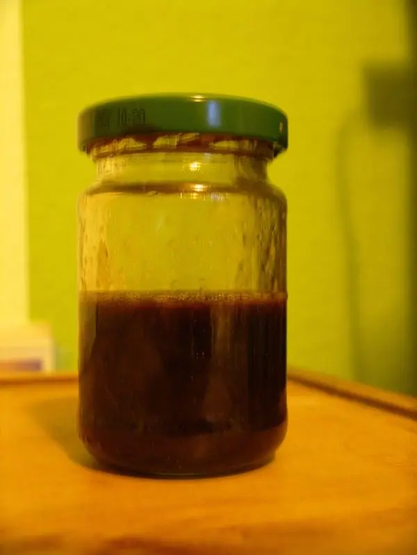 Ein Glas mit dunkler Flüssigkeit steht auf einem Holzbrett. Es könnte Essig-Öl als Möbelpolitur enthalten.