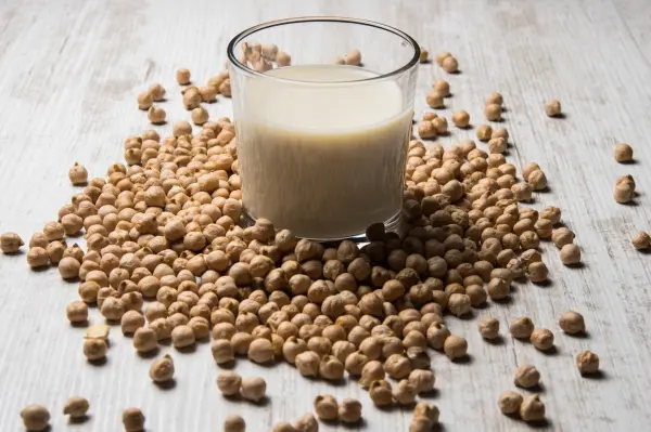 Ein Glas Soja-Drink steht auf einem Haufen von Sojabohnen und zeigt pflanzliche Alternativen zur Milch in einer hellen Umgebung.