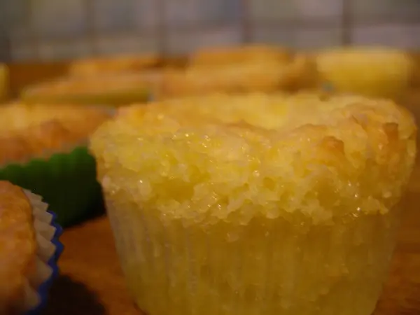 Nahaufnahme eines frisch gebackenen Muffins, der auf einem Holztisch steht. Im Hintergrund sind weitere Muffins zu sehen.