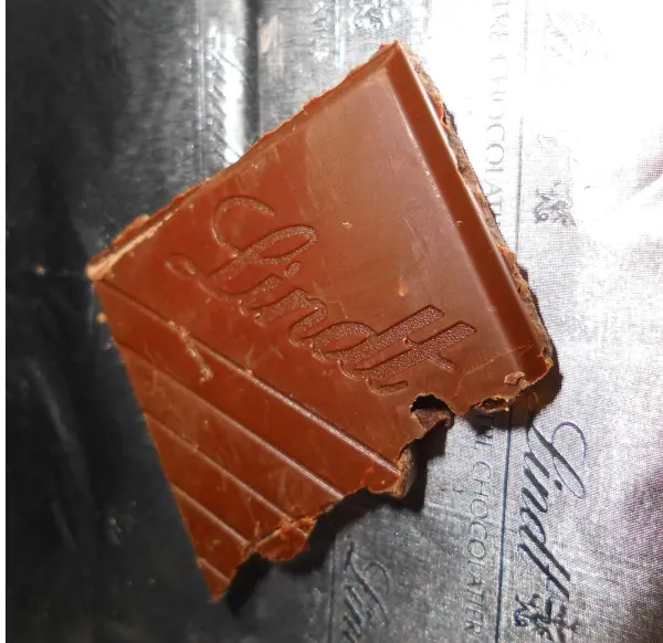Ein angebissenes Stück Lindt-Schokolade liegt auf einer Lindt-Verpackung mit dem eingeprägten Logo.