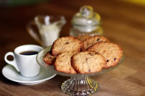 Ein Teller mit leckeren Cookies aus Müsliresten steht neben einer Tasse Kaffee auf einem Holztisch, gemütliche Atmosphäre.