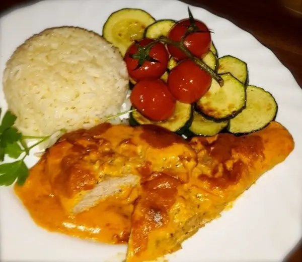 Schnitzel mit cremiger Sauce, gegrillte Zucchini und Cherrytomaten auf einem Teller mit Reis serviert.