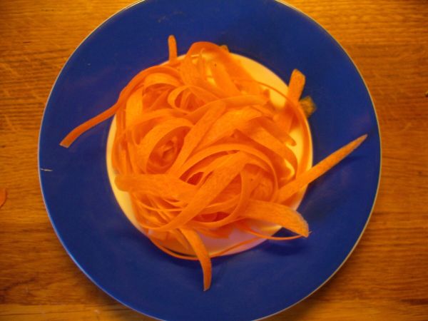 Eine Schüssel mit orangefarbenen, spiralförmigen Karottenstreifen liegt auf einem blauen Teller in einer Küchenumgebung.
