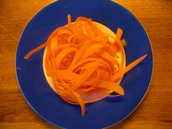 Eine Schüssel mit orangefarbenen, spiralförmigen Karottenstreifen liegt auf einem blauen Teller in einer Küchenumgebung.