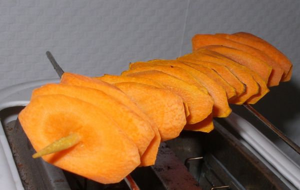 Möhrenchips werden auf einem Toaster zubereitet, während geschnittene Karottenscheiben auf einem Spieß angeordnet sind.