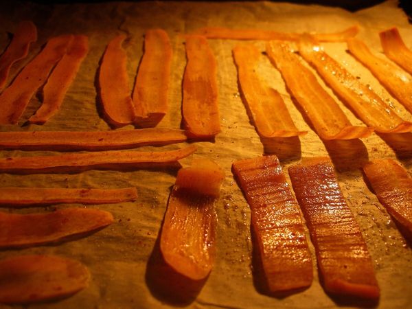 Möhrenchips liegen gleichmäßig auf Backpapier und werden im Backofen gebacken, während das Licht im Ofen leuchtet.