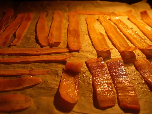 Möhrenchips liegen gleichmäßig auf Backpapier und werden im Backofen gebacken, während das Licht im Ofen leuchtet.