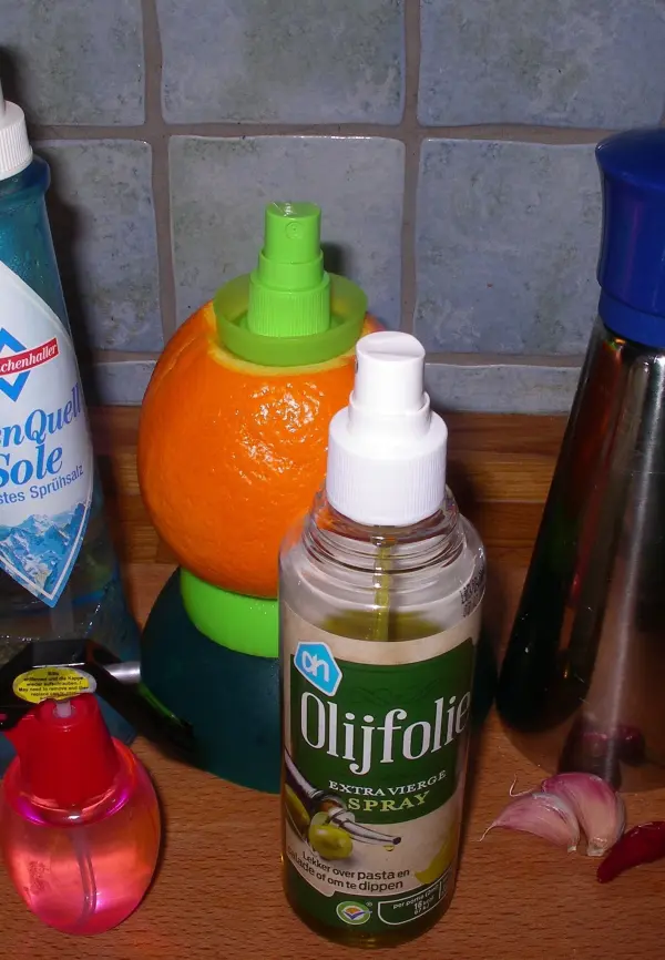 Ein Sprühflasche mit Olivenöl sprüht Gewürz in eine orangefarbene Zitruspresse, um das Essen zu würzen.