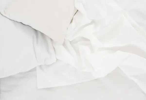 Weiße Bettwäsche und ein Kissen liegen auf dem Bett, bereit zur Reinigung von Blutflecken.