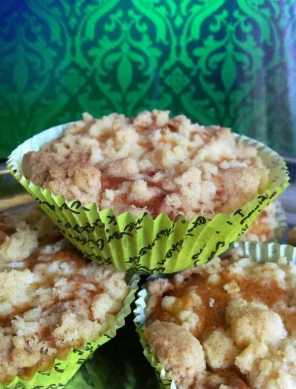 Goldene Apfel-Zimt Muffins mit Streuseln stehen auf einem Teller, umgeben von einem bunten, gemusterten Hintergrund.