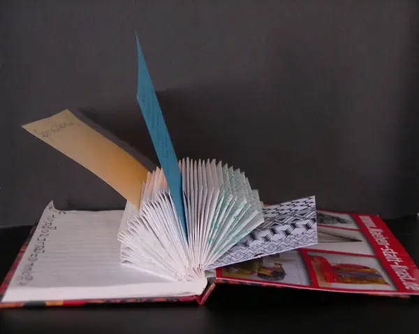Ein Notizhalter aus einer Kladde steht offen, mit bunten Seiten und einem kreativen Upcycling-Design, vor einem dunklen Hintergrund.