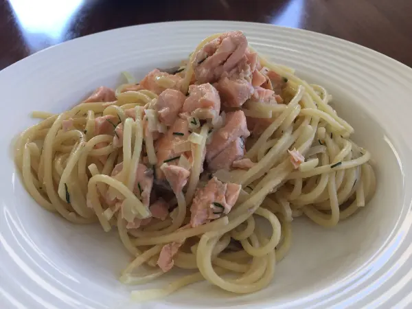 Nudeln mit Lachs liegen appetitlich auf einem weißen Teller, umgeben von einer Holzoberfläche.