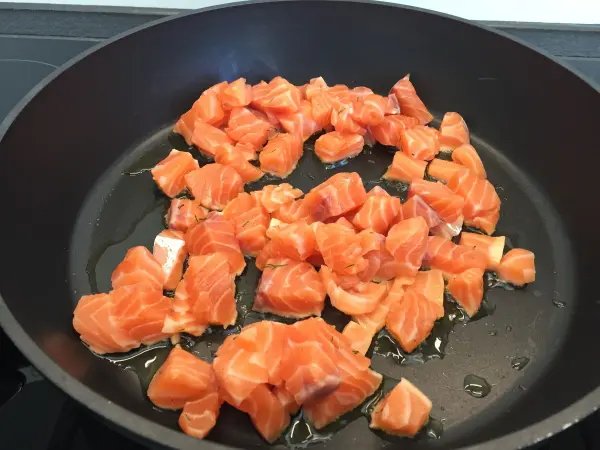 In einer Pfanne wird frischer Lachs in Würfeln angebraten. Der saftige Lachs bereitet sich darauf vor, in eine cremige Soße für die Nudeln integriert zu werden.