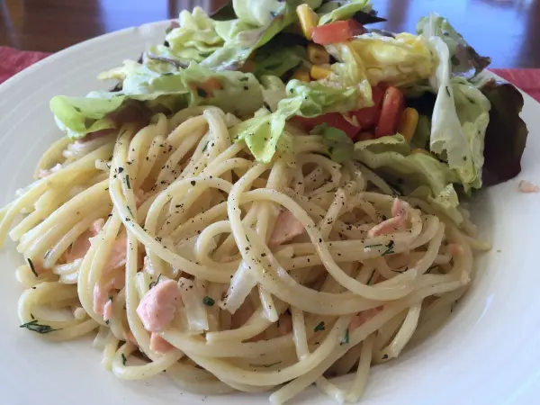 Spaghetti mit Lachs-Sahne-Soße werden auf einem Teller serviert, umgeben von frischem, buntem Salat.