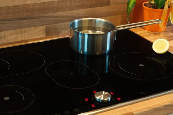 Ein Topf mit Wasser erhitzt sich auf einem modernen Induktionsherd in einer gemütlichen Küchenumgebung mit Holzregal.