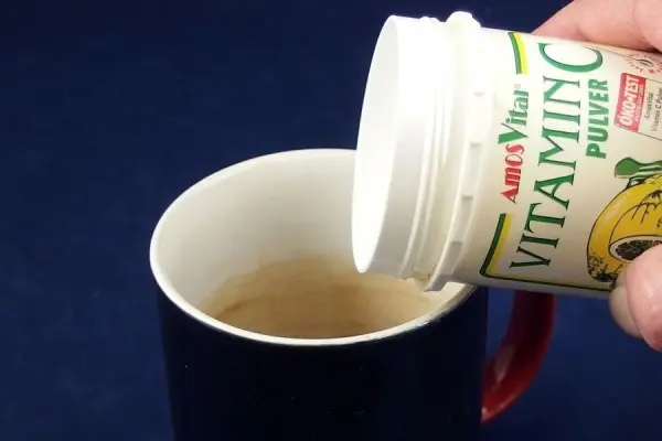 Ein Hand hält eine Dose mit Vitamin C Pulver und gießt es in eine Tasse, um Teeränder zu bekämpfen.