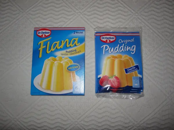 Verpackungen von Dr. Oetker Flana und Original Pudding, Vanille-Geschmack auf Tisch, zeigen cremige Puddingabbildungen.