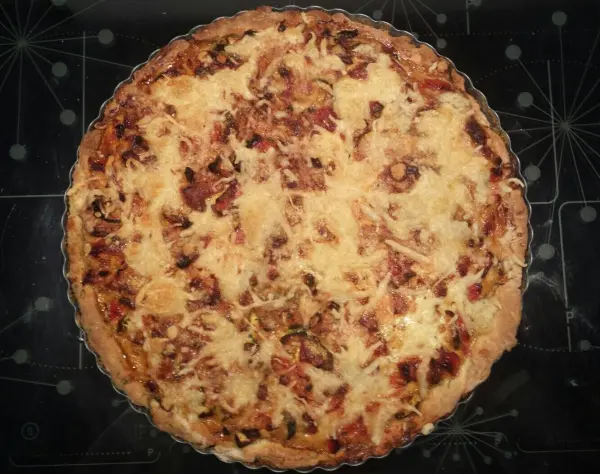 Eine glutenfreie Gemüse-Quiche liegt auf einem dunklen Blech, mit goldbraunem Belag und appetitlichen Gemüsestücken.