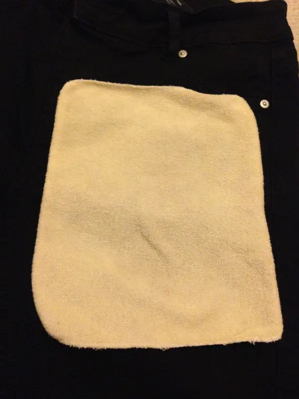 Ein abgerundetes, flauschiges Tuch liegt auf einer dunklen Jeans, um Knitterfalten unterwegs wegzuwischen.
