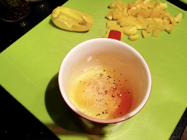 Ein Becher mit Rührei-Mischung steht auf einem grünen Schneidebrett, umgeben von geschnittenem Gemüse.