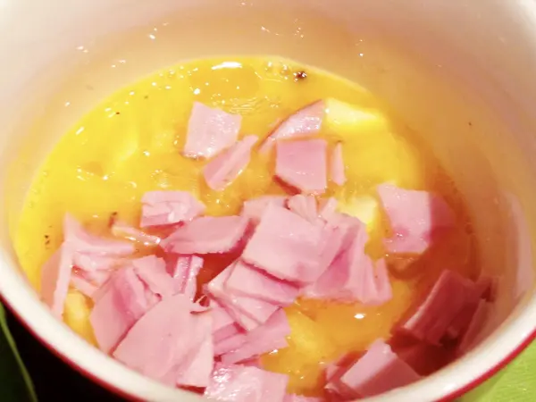 Ein Becher mit Rührei, angereichert mit Schinkenstücken, wird in einer Mikrowelle zubereitet.