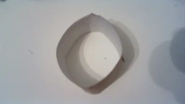 Eine flache, runde Flaschenmütze aus Papier liegt auf einem Tisch und zeigt eine geschwungene, äußere Kante.