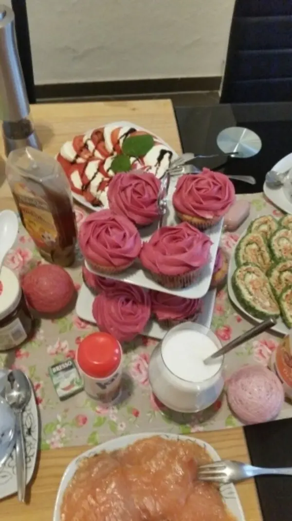 Eine Tortentafel mit frischen Cupcakes, die mit rosafarbenem Frischkäse-Frosting verziert sind, und verschiedenen Snacks.