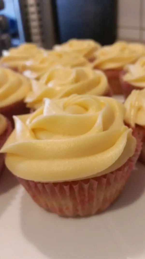 Leckere Cupcakes mit zartem Frischkäse-Frosting in Rosenform stehen auf einem Teller und laden zum Genießen ein.