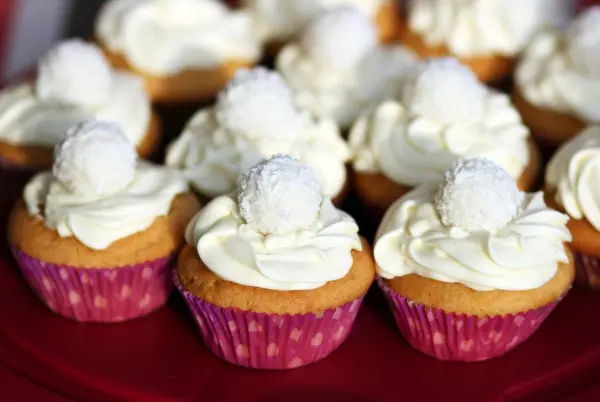 Muffins mit einer cremigen Topping-Schicht und einer süßen, runden Dekoration sind auf einem Platten arrangiert.