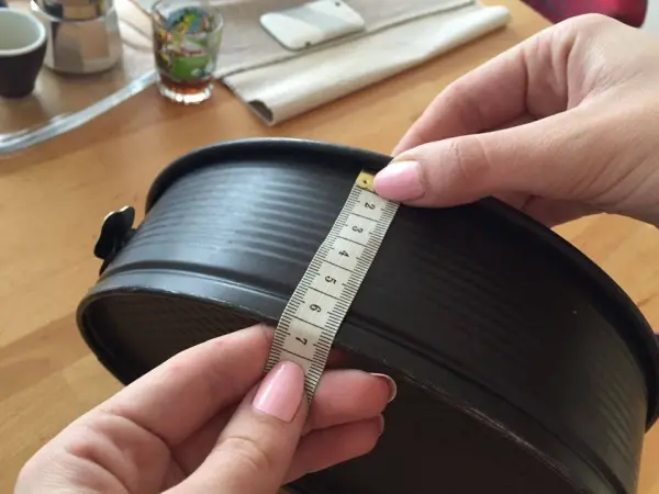 Eine Hand hält ein Maßband an einer Kuchenform, während sie die Größe überprüft, um einen perfekten Kuchen ohne Kuppe zu backen.