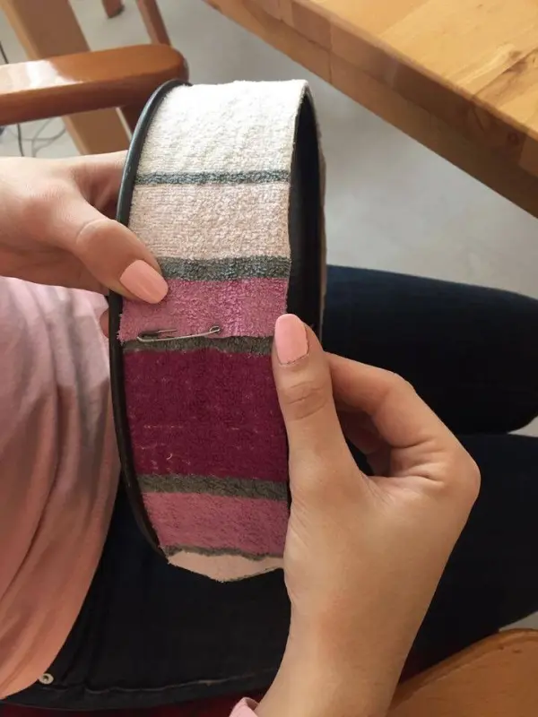 Eine Person hält eine mit buntem Stoff bezogene Backform, während sie in einem hellen Raum an einem Holztisch sitzt.