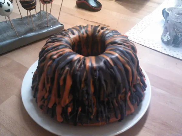Ein gruseliger Kuchen in Form eines Bundt-Kuchens, mit einer unheimlichen, orange-schwarzen Glasur, auf einem weißen Teller.