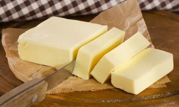 Eine frische Butter liegt auf einem Holzbrett, während ein Messer Stücke davon schneidet, um sie zu servieren.