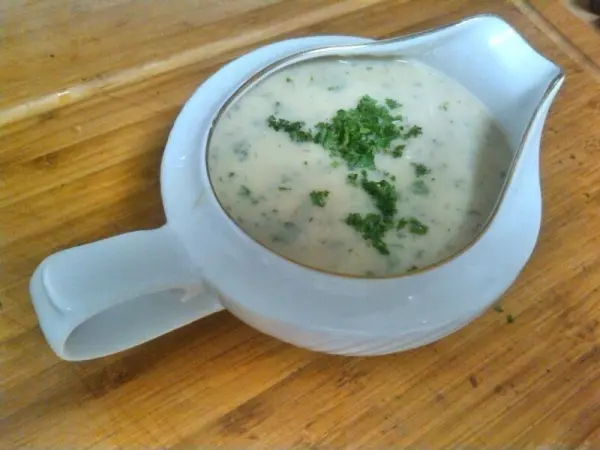 Eine weiße Gorgonzolasoße mit frischer Petersilie wird in einer eleganten Sauciere auf einem Holzbrett serviert.