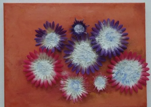 Bunte Blütenblätter einer Plastikblume gruppieren sich lebhaft auf einer orangefarbenen Acrylfläche, die den Raum erhellt.