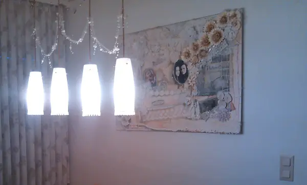Ein Acrylbild mit Blütenblättern einer Plastikblume hängt an der Wand, beleuchtet von einer modernen Lampe im Raum.