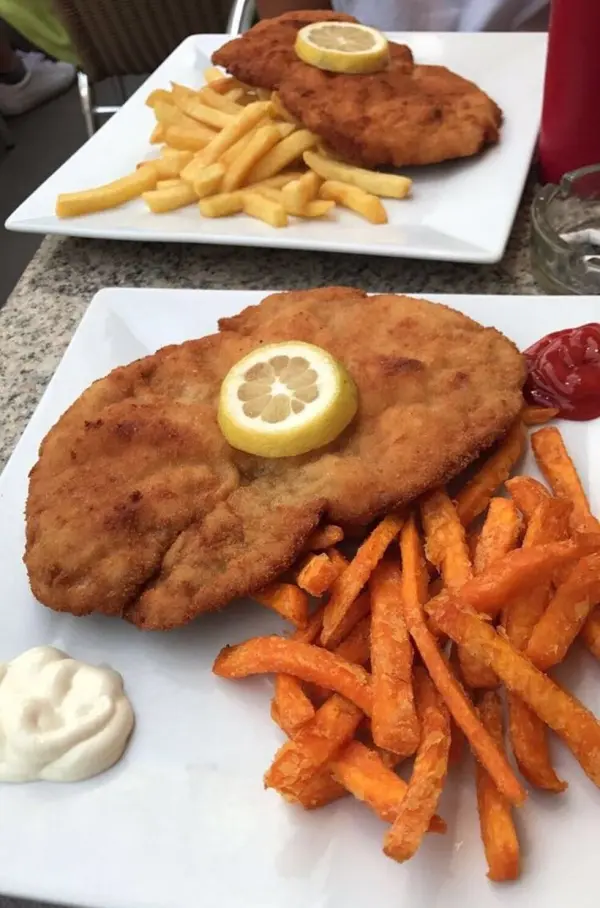 Ein großes Schnitzel mit Zitrone und Beilagen von Pommes und Süßkartoffelpommes auf einem Teller, serviert in einem Restaurant.