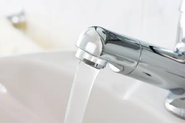 Ein glänzender Wasserhahn gibt Wasser ab, während er in einem modernen Badezimmer auf einer weißen Waschbeckenfläche steht.