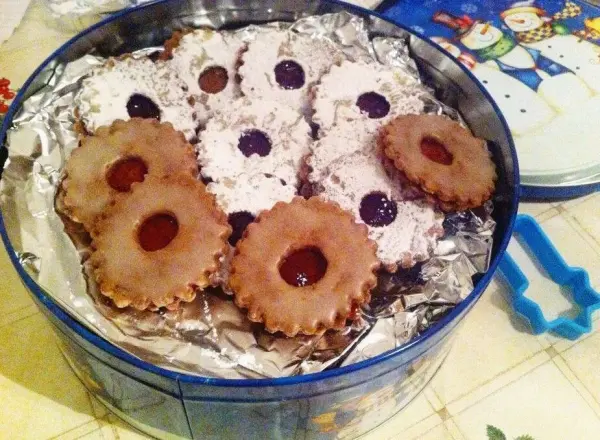 Zimt-Kirsch-Plätzchen liegen ordentlich in einer runden Dose und zeigen eine Mischung aus hellen und dunklen Keksen, verziert mit Marmelade.