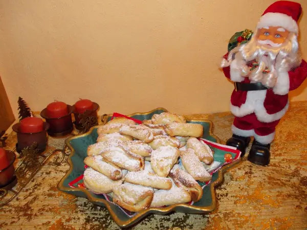 Auf einem Teller liegen gefüllte Muschelplätzchen, umgeben von festlichen Kerzen und einer Weihnachtsmannfigur im Hintergrund.